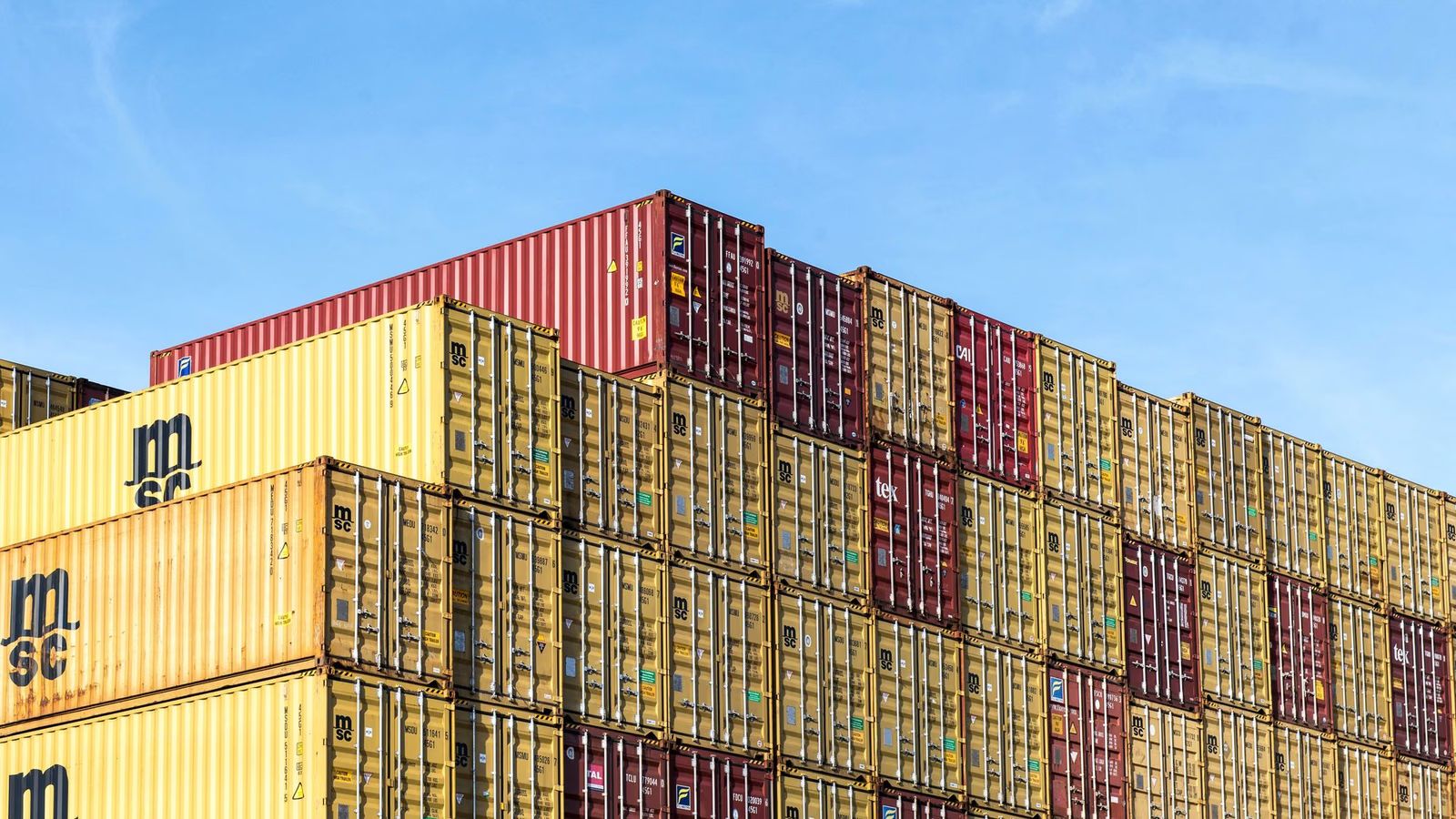 Stacked yellow and red shipping containers against a blue sky